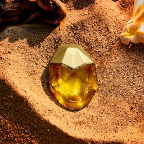 Golden gem-shaped perfume bottle on sand.