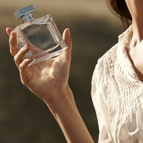 Woman holding a clear perfume bottle.